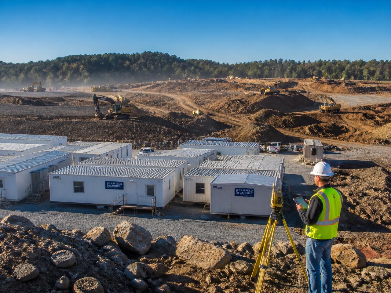 Site office trailers in the foreground of a large earthworks construction site with excavators working