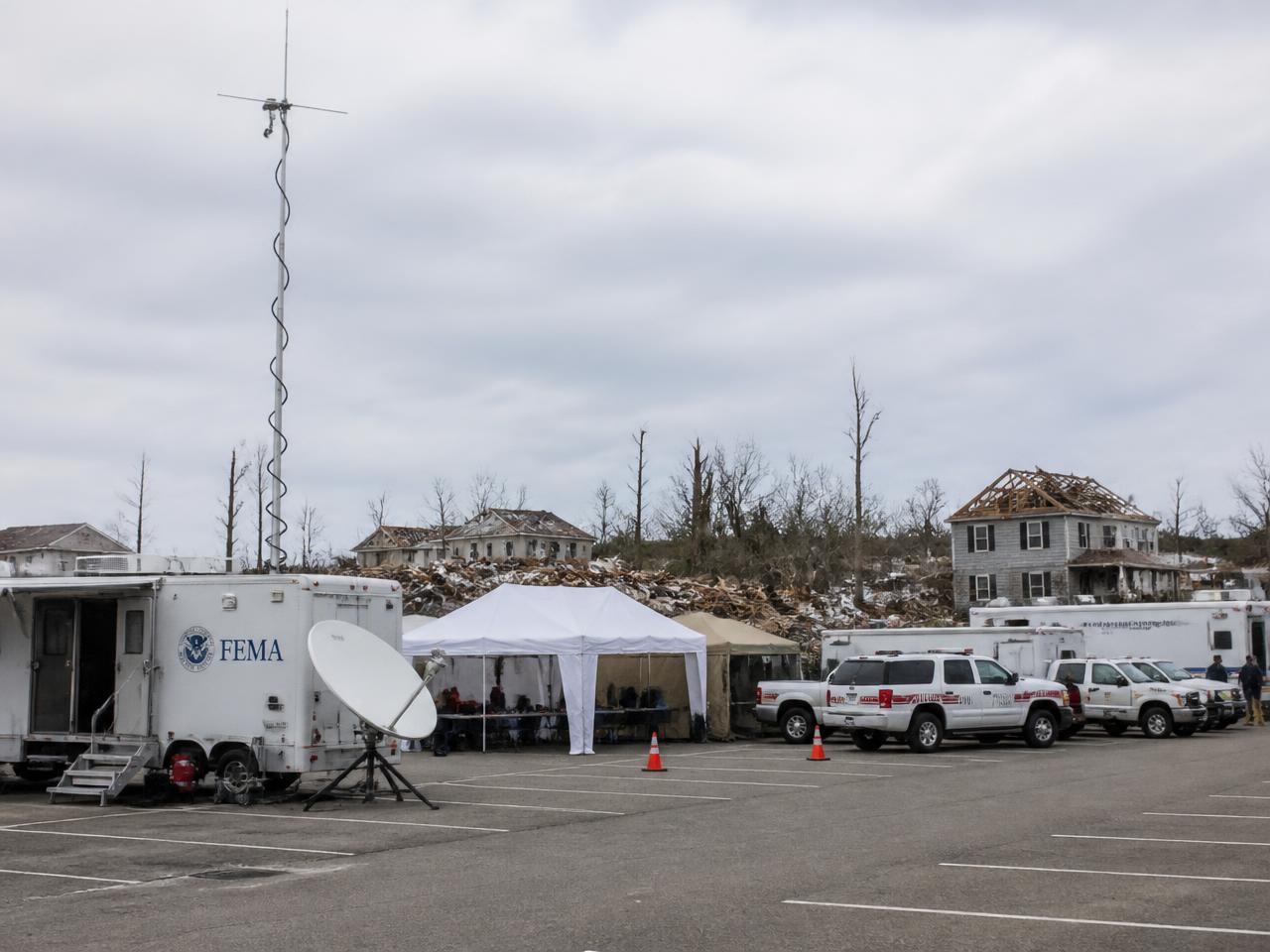 Emergency response vehicles, tents, a portable antenna mast and a satellite dish at a disaster relief staging area