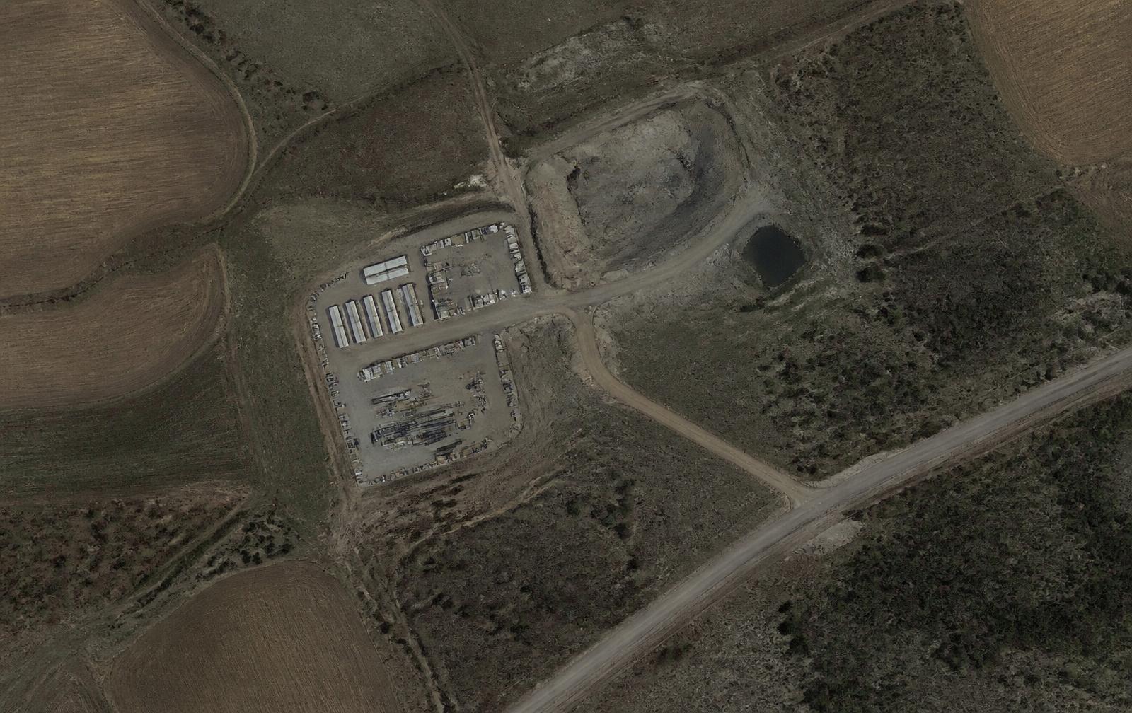 Satellite view of a rural jobsite with site trailers, a laydown yard, an excavated pit, and a haul road